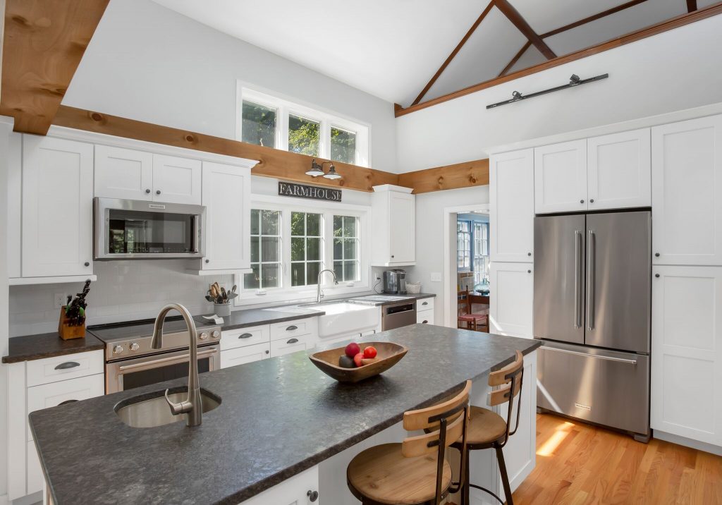 Modern white kitchen with stainless steel appliances, island with sink, and a bowl of fruit on the countertop.