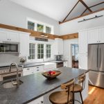 Modern white kitchen with stainless steel appliances, island with sink, and a bowl of fruit on the countertop.