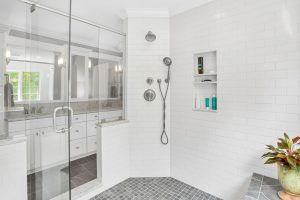 Modern walk-in shower with white subway tiles, built-in shelves, and silver fixtures, next to a double-sink vanity.