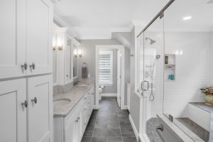 Modern bathroom with double sinks, large mirror, glass shower, gray tile floor, and white cabinets.