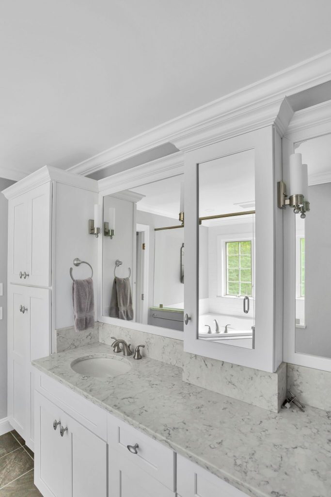 White bathroom vanity with marble countertop, dual mirrors, two wall lights, and gray hand towels on towel rings.