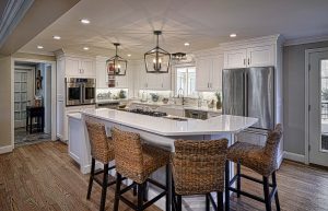 Modern kitchen with white cabinets, stainless steel appliances, island with cooktop, and four woven barstools.