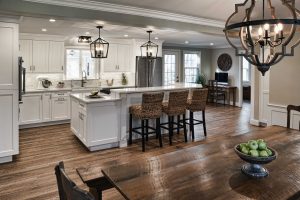 Modern kitchen with white cabinets, a large island with barstools, and a wooden dining table with a bowl of green apples.