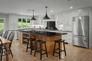 Modern kitchen with white cabinets, stainless steel appliances, island with black countertop, and three stools.