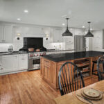 Spacious kitchen with white cabinets, black countertops, a large island, and wooden dining table with chairs.