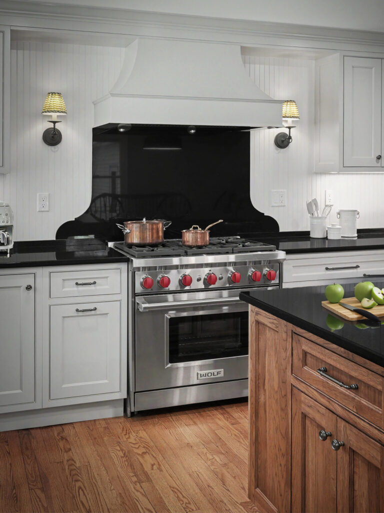 Modern kitchen with stainless steel stove, black backsplash, white cabinets, and a wooden island with green apples.