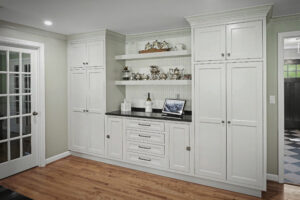 White built-in cabinets with shelves display silver teapots and dishes above a black countertop and wooden floor.