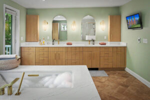 Modern bathroom with double sinks, wood cabinets, marble countertops, and mounted TV on a green wall.