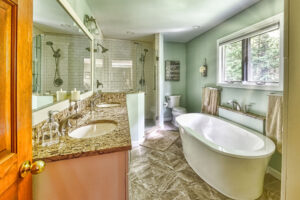 Modern bathroom with double sinks, a freestanding tub, glass shower, and window overlooking greenery.