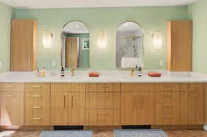 Double bathroom vanity with wooden cabinets, two mirrors, gold fixtures, and wall sconces against a green wall.