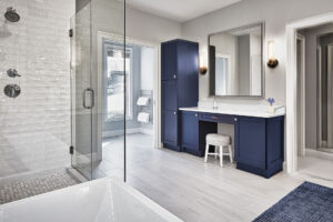 Modern bathroom with a glass shower, blue vanity, large mirror, wall sconces, and white tile flooring.