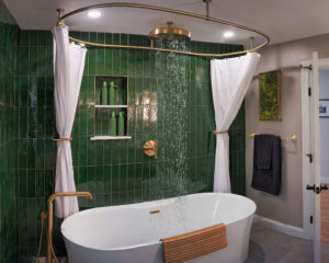 Modern bathroom with green tiled walls, a white freestanding tub, and a ceiling-mounted rainfall showerhead with curtains.