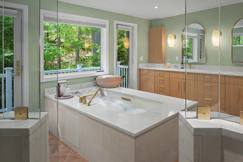Modern bathroom with soaking tub, large windows, wood cabinets, double sinks, and views of green trees outside.