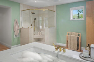 Modern bathroom with a soaking tub, gold fixtures, glass shower, towel rack, and light green walls.