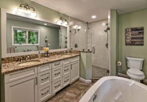 Modern bathroom with double-sink vanity, granite countertop, glass shower, bathtub, and toilet under wall art.