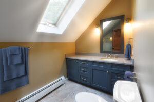 Bathroom with blue cabinets, gold walls, skylight, wall-mounted lights, towel rack, and a mirror above the sink.
