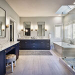 Modern bathroom with navy cabinets, dual sinks, a glass shower, freestanding tub, and large windows letting in natural light.