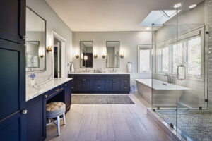 Modern bathroom with navy cabinets, dual sinks, a glass shower, freestanding tub, and large windows letting in natural light.