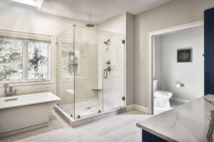 Modern bathroom with glass shower, freestanding tub, large window, and separate toilet room.