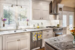 This is a bright kitchen with white cabinets, marble countertops, stainless steel appliances, and sunlight streaming in.
