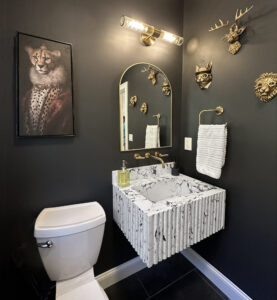 Modern bathroom with black walls, marble sink, gold fixtures, animal head wall decor, and a cheetah portrait.