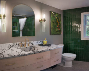 Modern bathroom with green tile walls, large mirror, marble countertop, and gold fixtures.