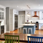 Modern kitchen with white cabinets, stainless appliances, island seating, and a wooden dining table with colorful chairs.
