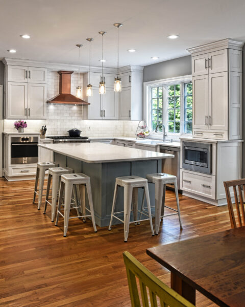 Modern kitchen with white cabinets, a central island with stools, wood floors, and large windows letting in natural light.