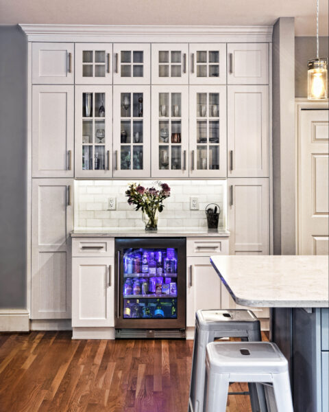 Modern kitchen with white cabinets, marble countertop, mini fridge with drinks, and purple lighting.