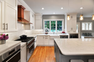 Modern kitchen with white cabinets, stainless appliances, an island, wood floors, and large window overlooking yard.