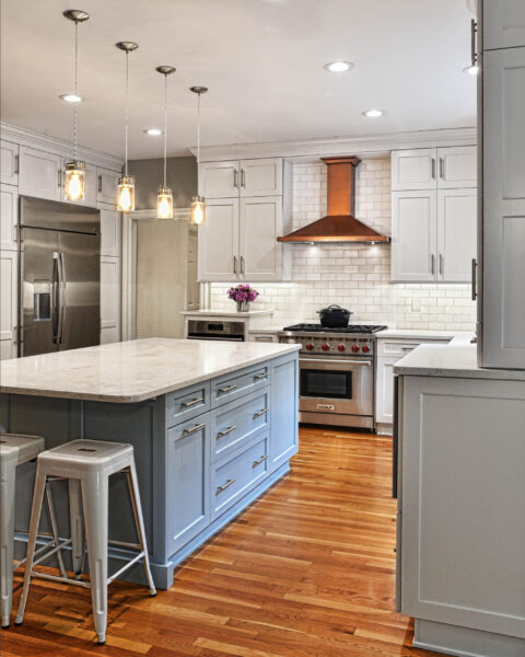 Modern kitchen with white cabinets, stainless steel appliances, wood floor, and marble island with metal stools.