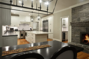 Modern kitchen with white cabinets, island, stainless steel appliances, stone fireplace, and wood floors.