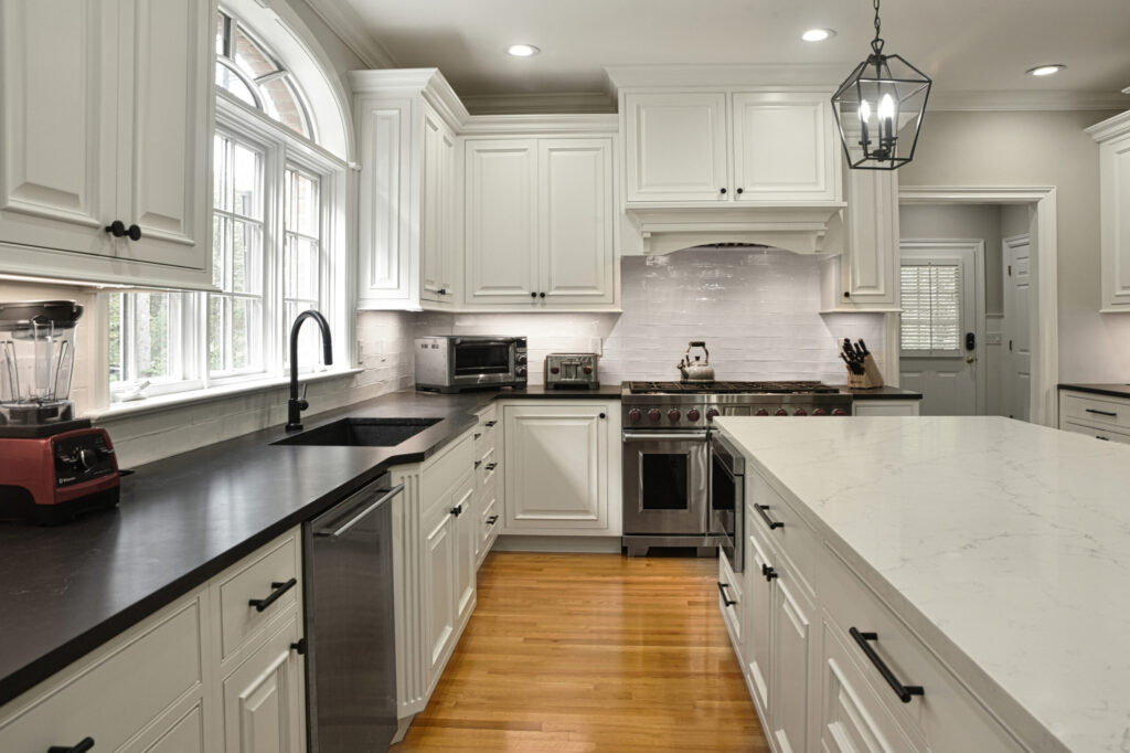 Modern kitchen with white cabinets, black countertops, stainless appliances, and a central island with marble surface.