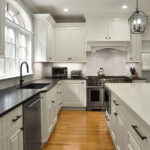 Modern kitchen with white cabinets, black countertops, stainless appliances, and a central island with marble surface.