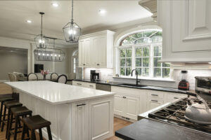 Modern kitchen with white cabinets, marble island, black countertops, pendant lights, and large arched window.