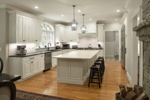 Modern kitchen with white cabinets, island with stools, pendant lights, hardwood floor, and stainless steel appliances.
