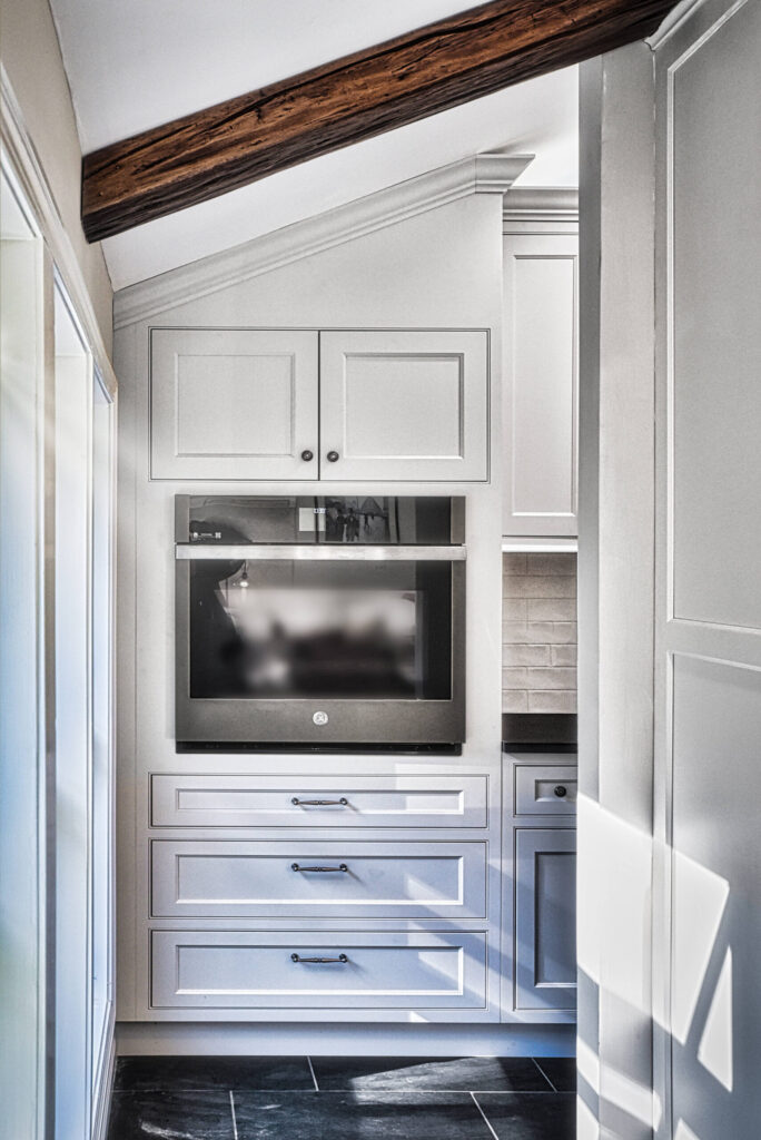Small modern kitchen with white cabinets, built-in oven, under-cabinet microwave, and dark tile floor.