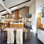 Spacious modern kitchen with a wooden dining table, island, chevron backsplash, and large windows letting in natural light.