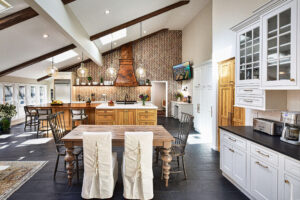 Spacious modern kitchen with a wooden dining table, island, chevron backsplash, and large windows letting in natural light.