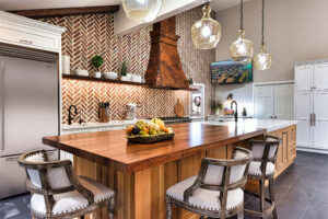 Spacious kitchen with wood island, herringbone brick backsplash, pendant lights, and bowl of fruit on the counter.
