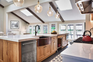 Modern kitchen with wood island, farmhouse sink, pendant lights, skylights, and a red kettle on the stove.