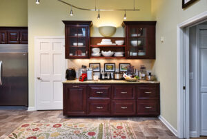Kitchen area with dark wood cabinets, countertop appliances, dishes on shelves, and framed art on backsplash.