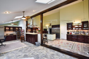 Spacious open kitchen with dark wood cabinets, light countertops, stainless appliances, and patterned rugs on tiled floor.