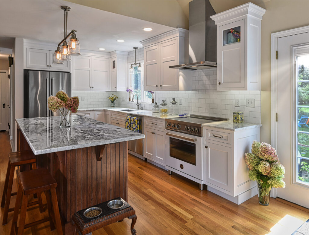 Modern kitchen with white cabinets, stainless steel appliances, marble island, and wooden floor.