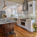 Modern kitchen with white cabinets, stainless steel appliances, marble island, and wooden floor.