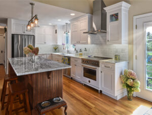 Modern kitchen with white cabinets, stainless steel appliances, marble island, and wooden floor.