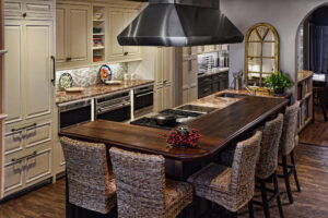 Modern kitchen with a wooden island, woven bar stools, stainless steel hood, and cream cabinets.