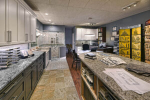 A kitchen and bath showroom displays tile, cabinet samples, blueprints, and design materials on counters and walls.