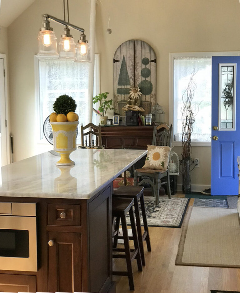Kitchen with a marble island, yellow vase of lemons, blue door, and cozy decor in natural light.